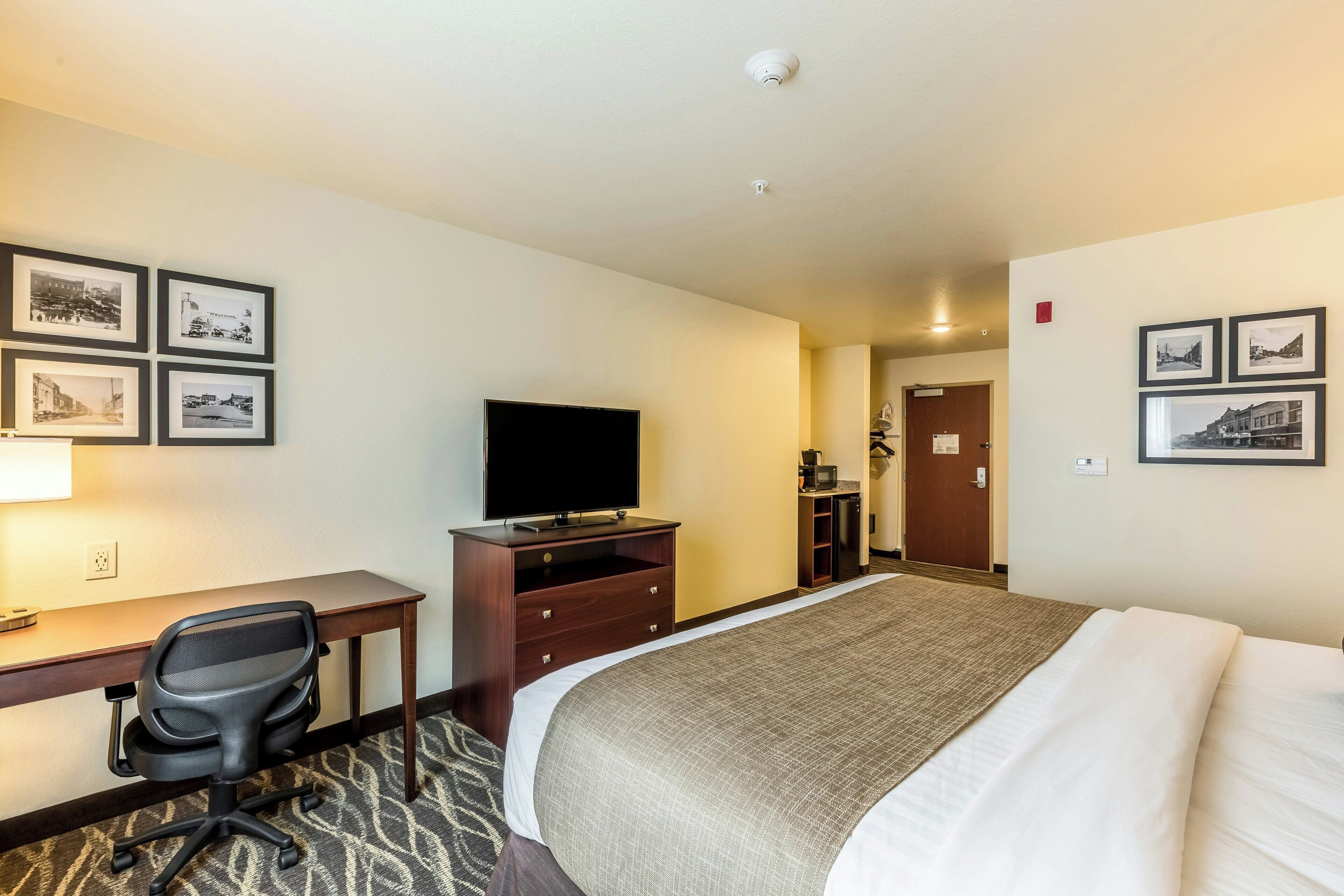 Habitación de hotel con cama, escritorio y silla, televisor y cuadros en las paredes.