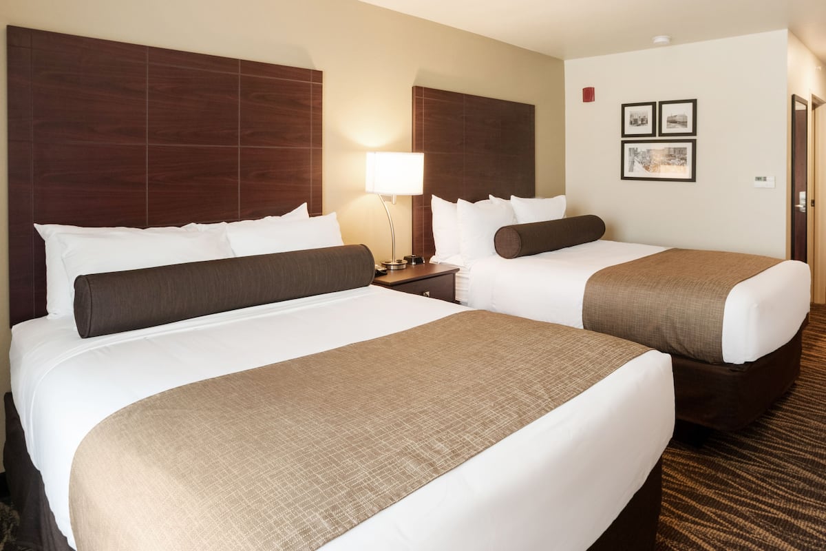 A hotel room with two beds, a nightstand, a lamp, and framed pictures on the wall.