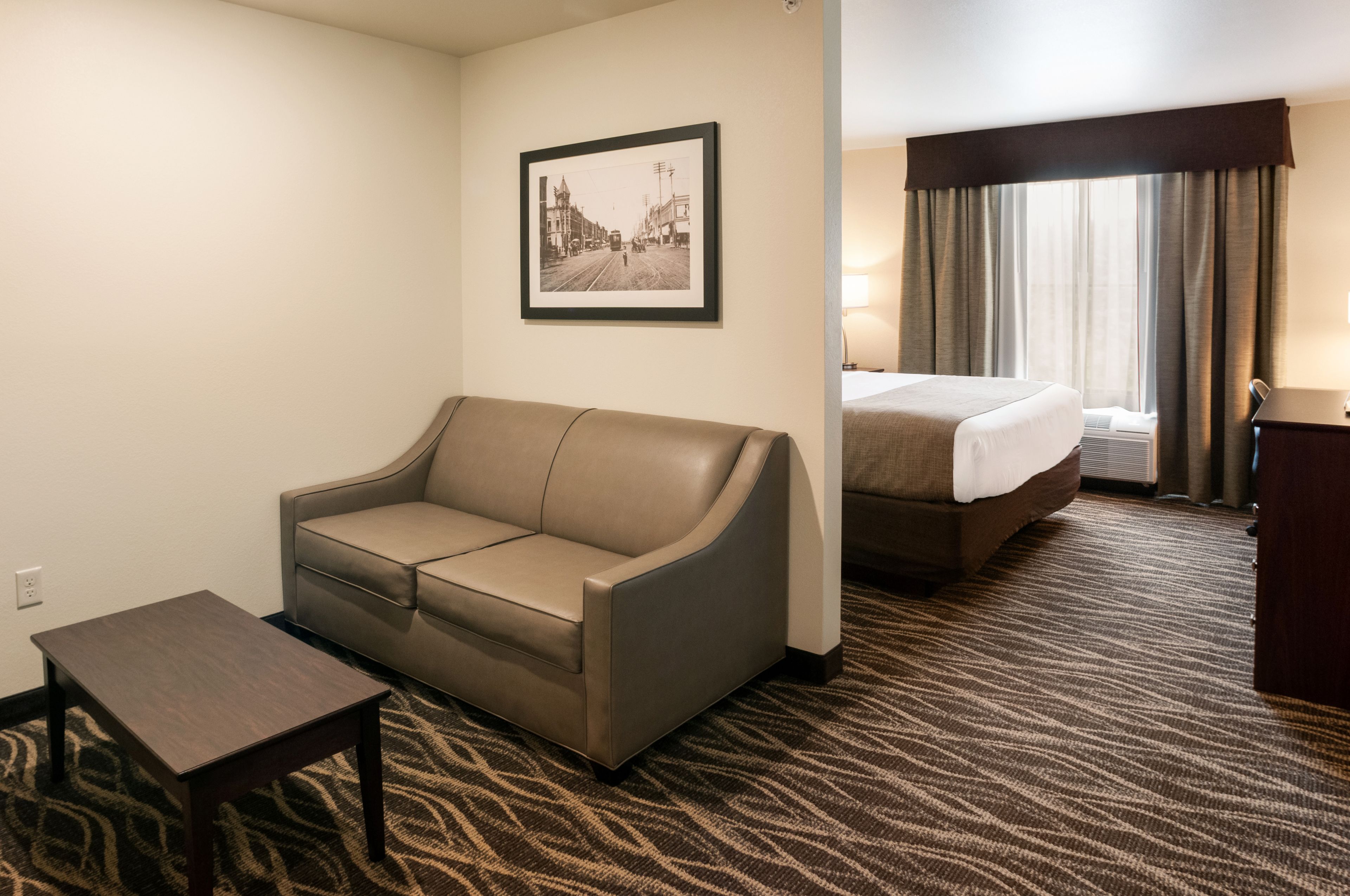 Habitación de hotel con sofá, una mesita, cama y un cuadro en la pared.