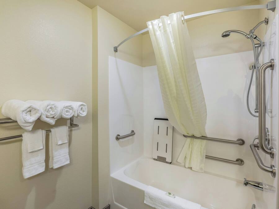 A bathroom with a bathtub, shower, and handrails.