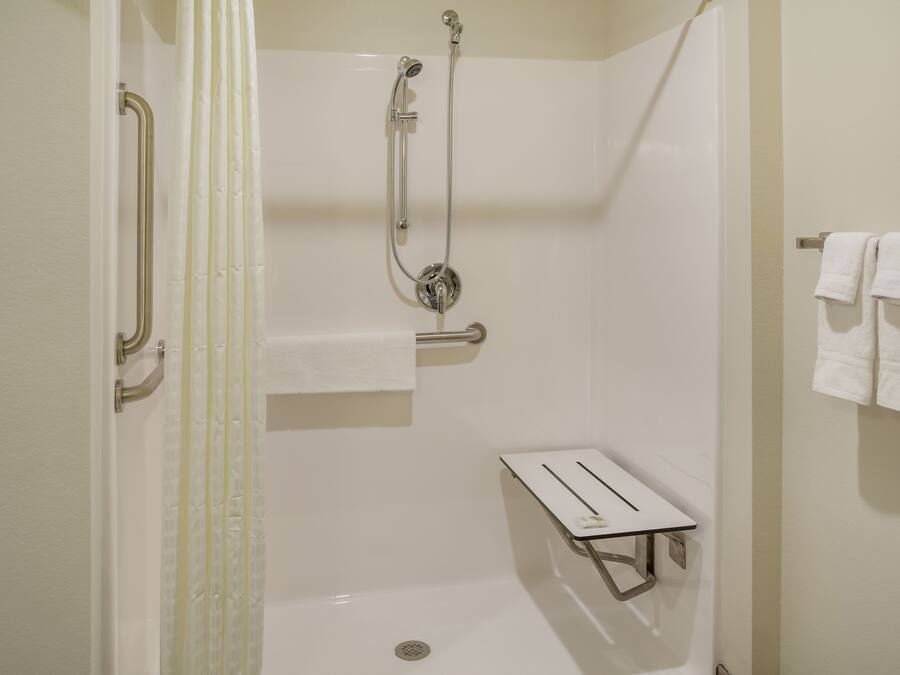 A walk-in shower with a handheld showerhead, a handheld showerhead, a towel rack with two towels, and a small shelf with a towel.