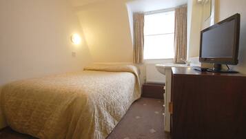 A small, neatly arranged bedroom with a bed, a dresser, a television, and a window with curtains.