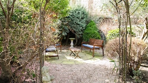 A garden with a wooden bench, a table, and a statue. - Jesmond Hotel (London)