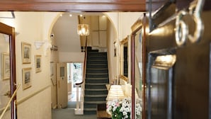 A hallway with a staircase, framed pictures on the walls, and a lamp on a table. - Jesmond Hotel (London)