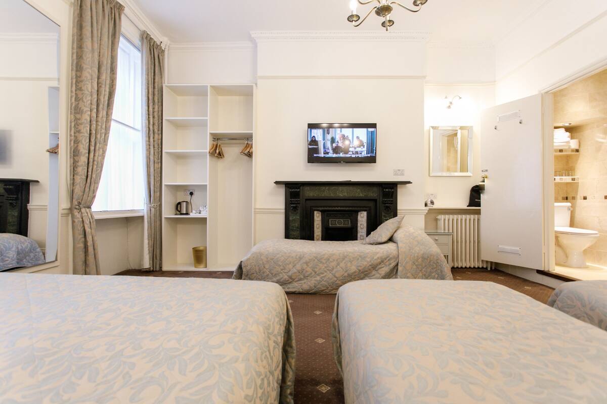 A hotel room with two beds, a television, a fireplace, a mirror, and a bathroom.