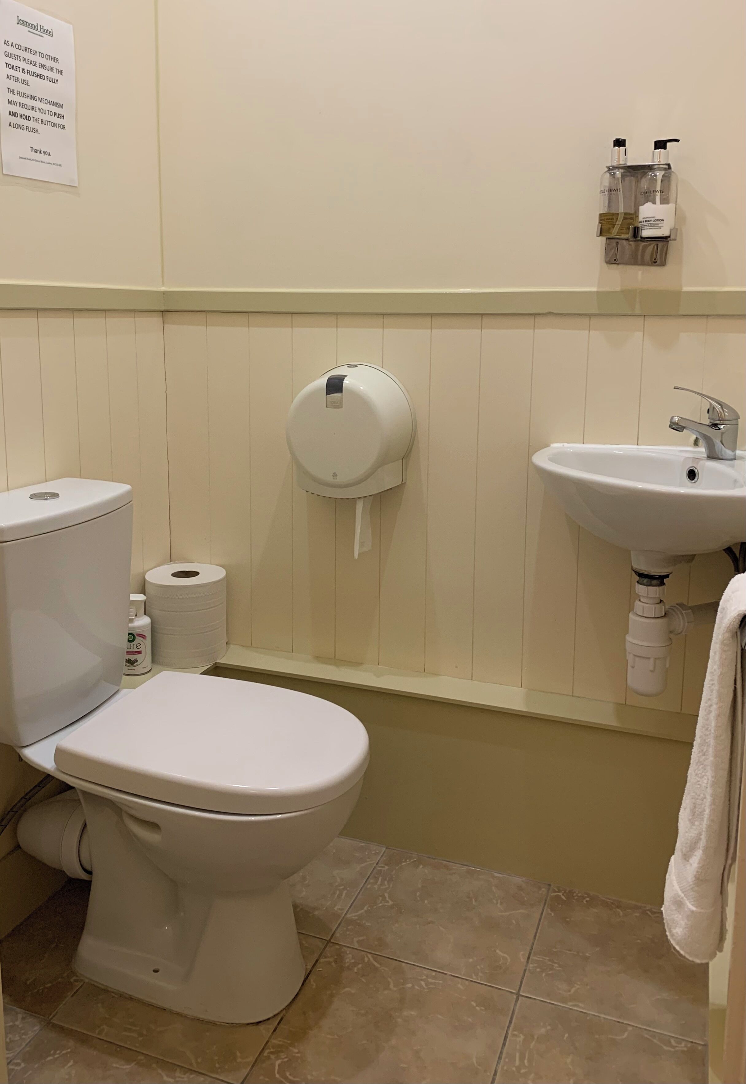 Un baño con inodoro, papel higiénico, gel antibacterial y lavamanos.