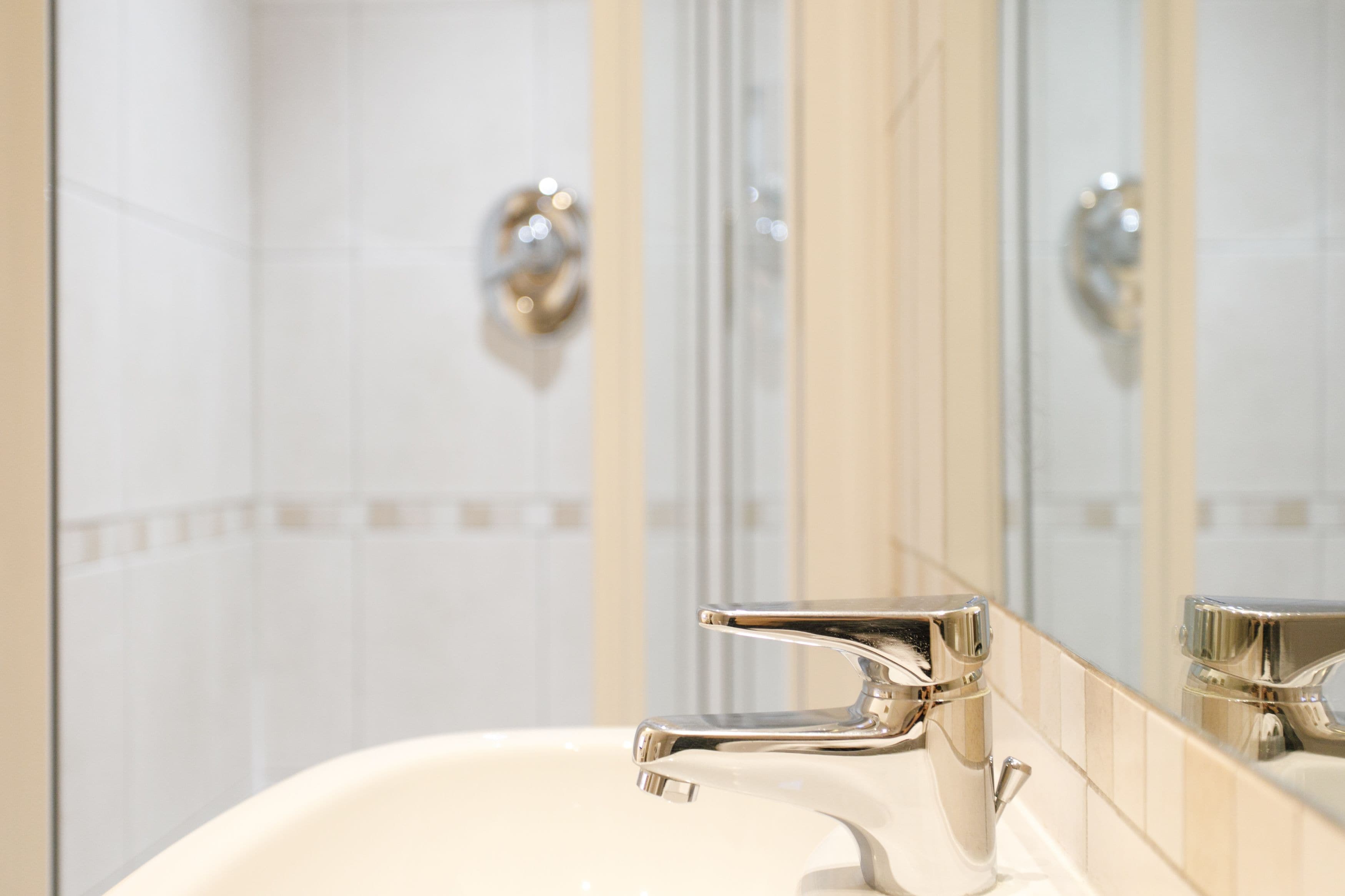 Un baño con grifería cromada, un espejo y paredes de azulejos.
