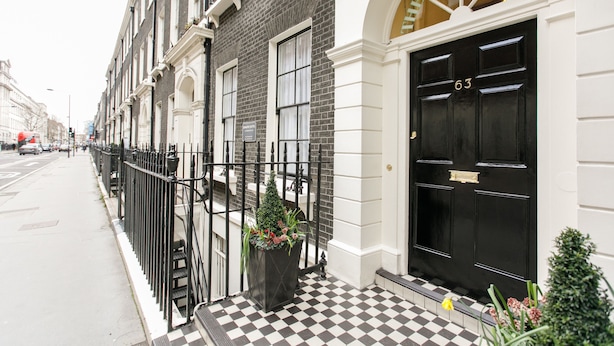 A row of townhouses with black doors, a checkered floor, and a black metal fence. - Jesmond Hotel (London)