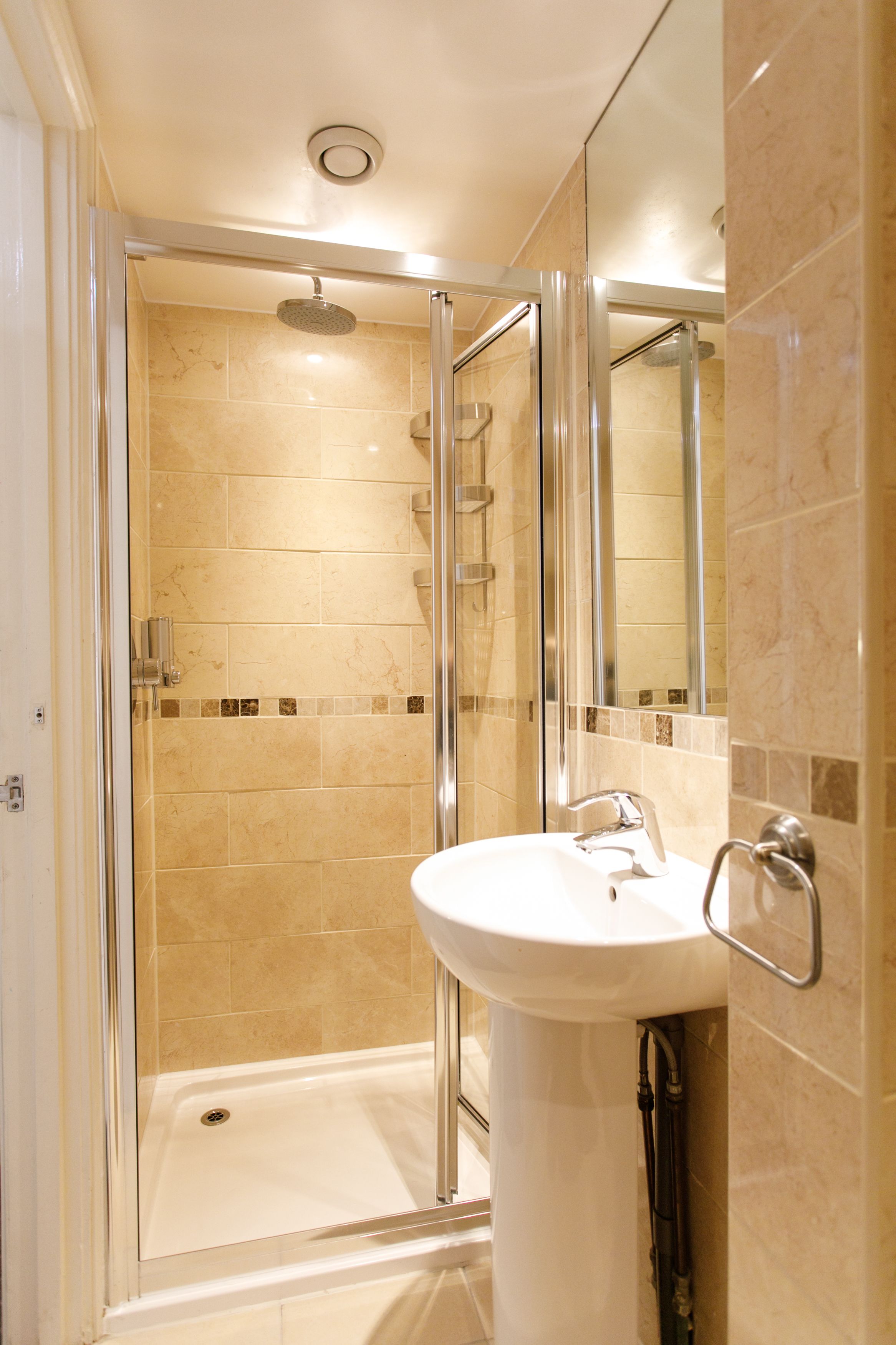 Un baño moderno con ducha de mampara de vidrio, lavamanos pedestal y espejo.