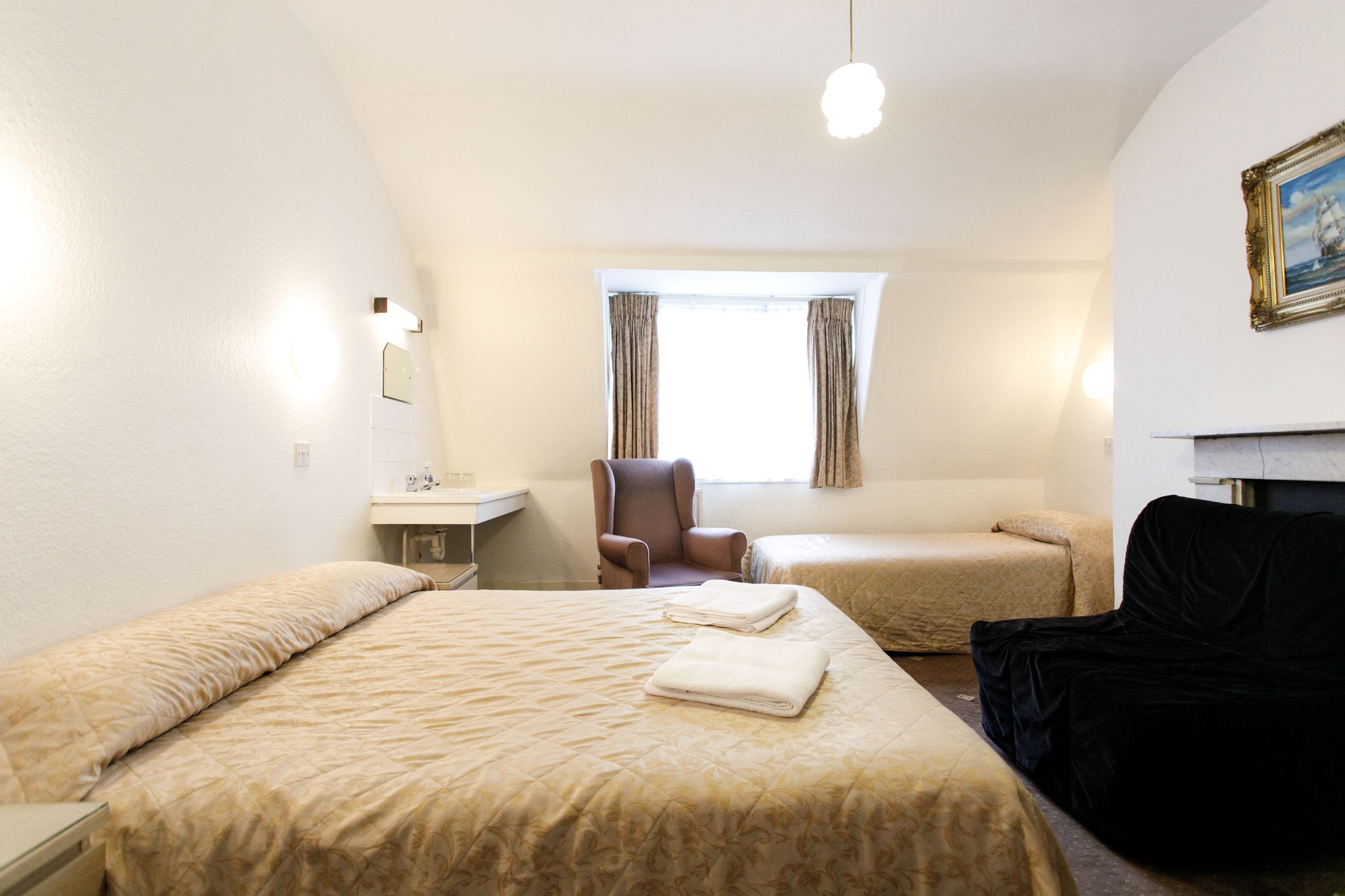 Une chambre d’hôtel avec deux lits, un bureau, une chaise et un canapé noir.