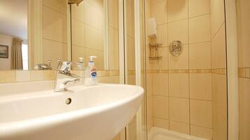Un baño con lavamanos blanco, un espejo, dispensador de jabón y zona de ducha.