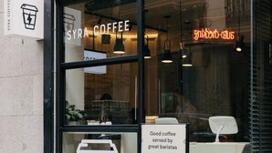 A coffee shop with a glass storefront, a neon sign, and a signboard advertising good coffee served by great baristas. - Select Sol (Madrid)
