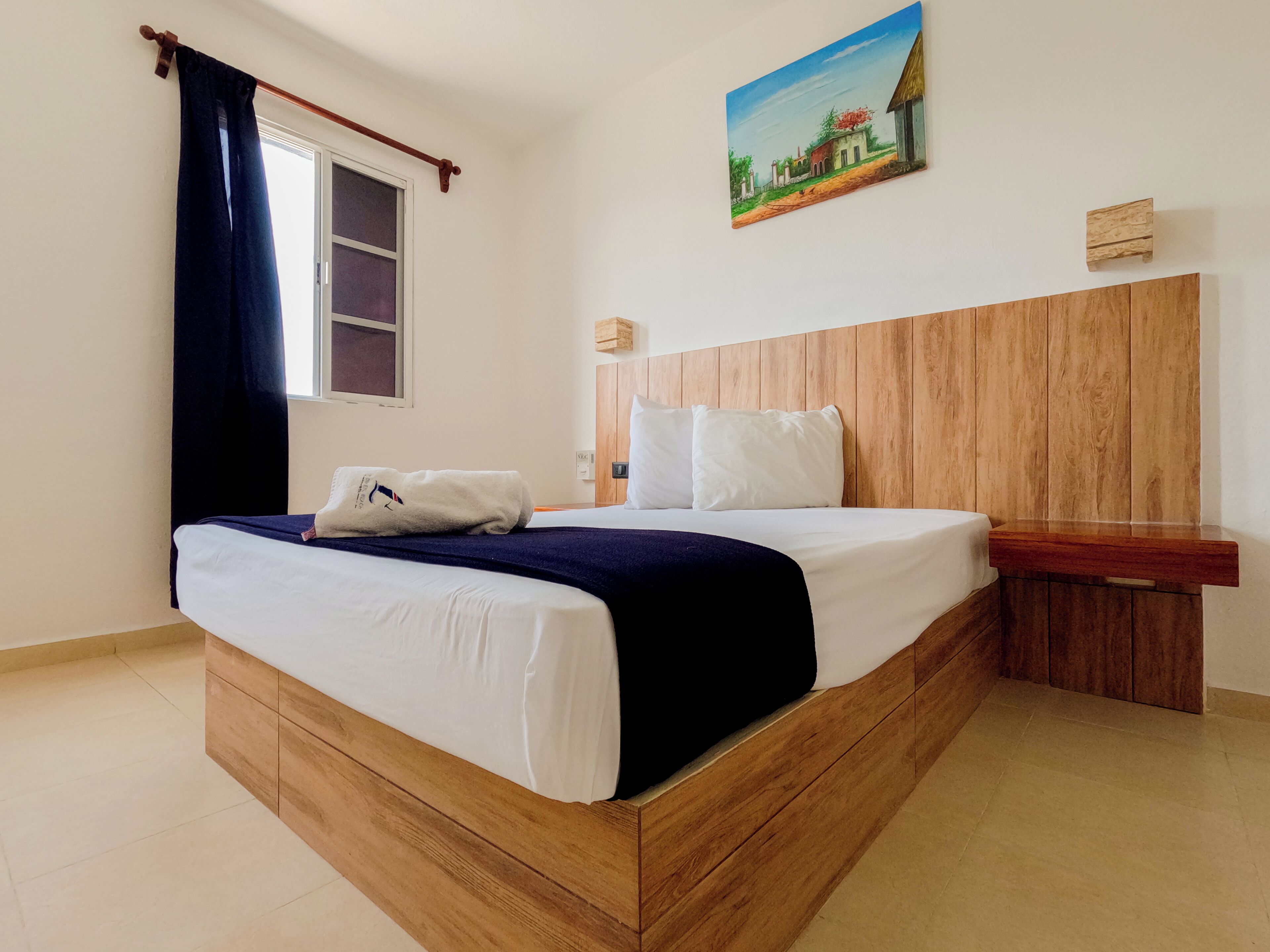 Een hotelkamer met een houten bed, wit beddengoed, een schilderij aan de muur en een raam met gordijnen.