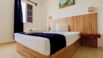 Een hotelkamer met een houten bed, wit beddengoed, een schilderij aan de muur en een raam met gordijnen.