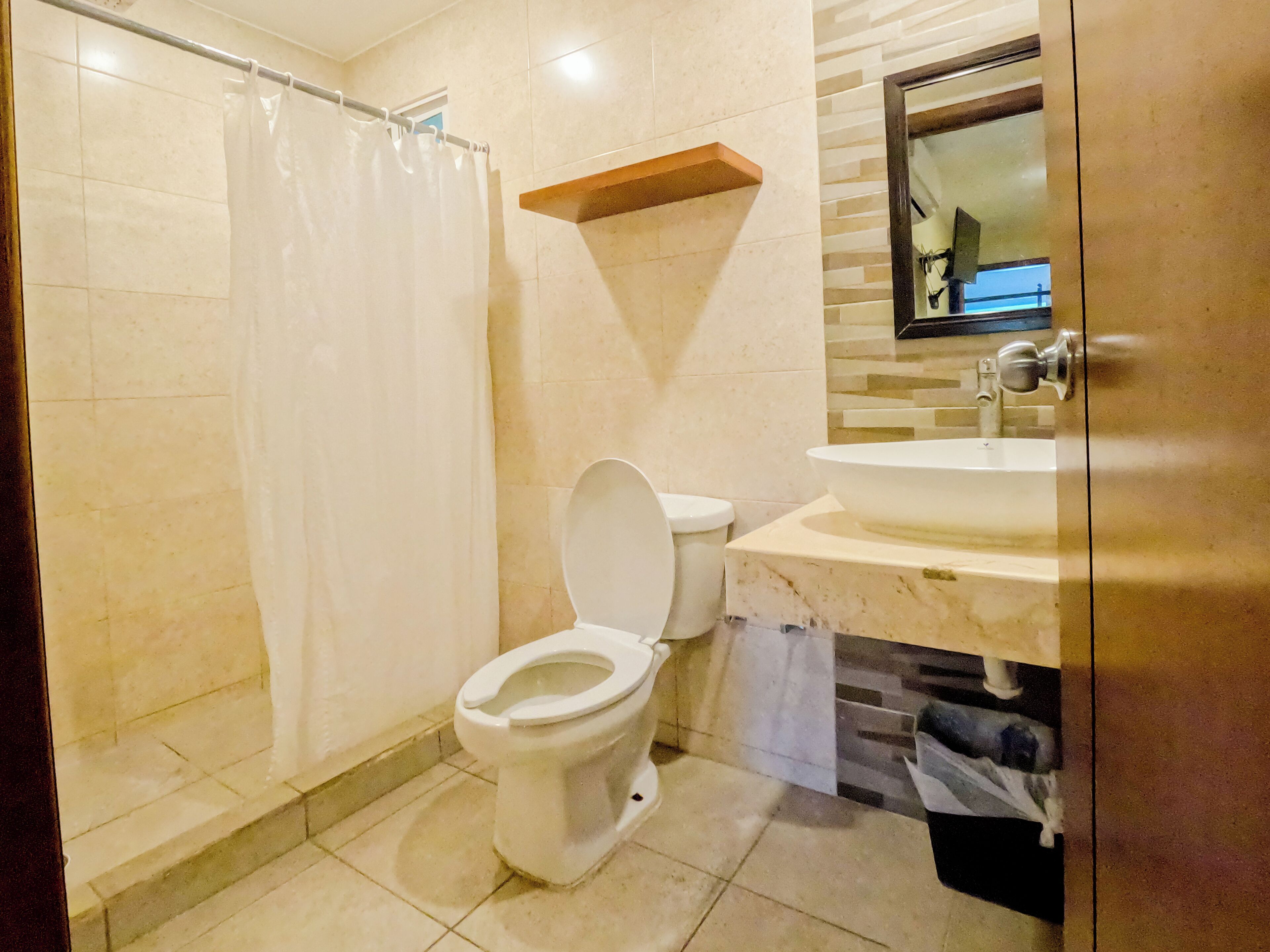 A bathroom with a toilet, a shower curtain, a sink, and a mirror.
