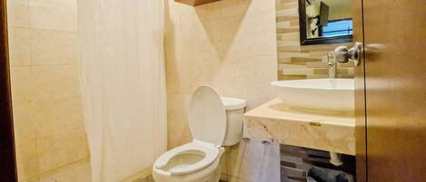 A bathroom with a toilet, a shower curtain, a sink, and a mirror.