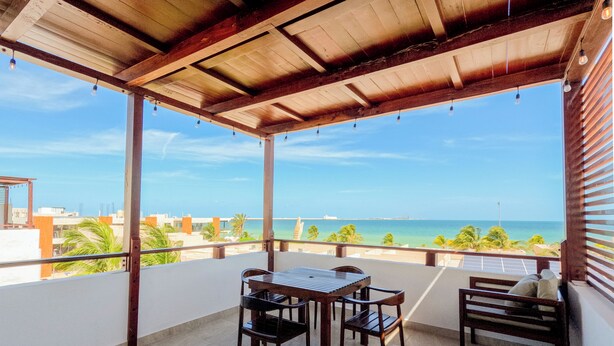 A covered outdoor area with a table and chairs, a view of the ocean, and a clear sky. - Progreso Beach Hotel (Progreso)