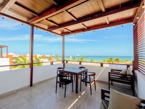 A covered outdoor area with a table and chairs, a view of the ocean, and a clear sky.