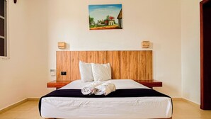 A neatly made bed with white linens and rolled towels, a wooden headboard, and a painting of a rural landscape on the wall. - Progreso Beach Hotel (Progreso)