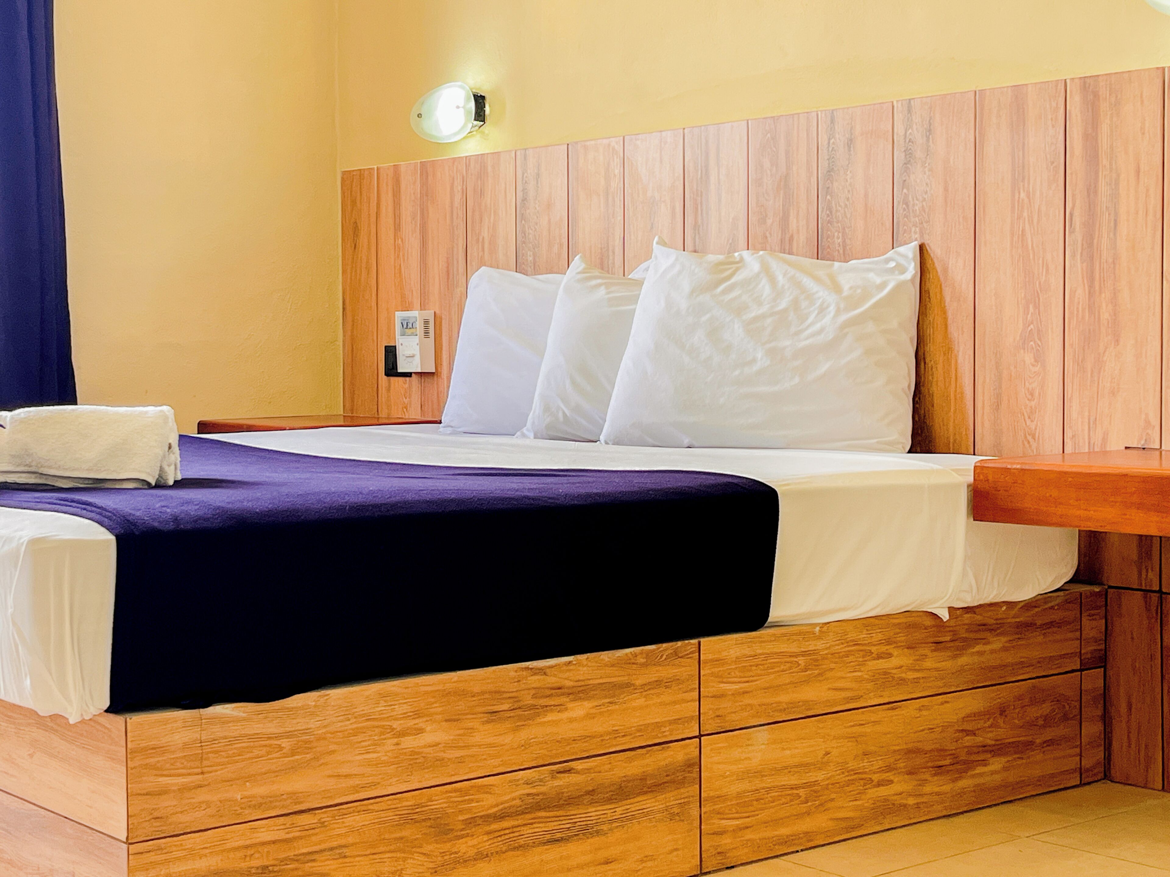 A hotel room with a wooden headboard, a bed with white linens, a purple bedspread, and a white towel on the side.