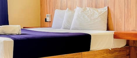 A hotel room with a wooden headboard, a bed with white linens, a purple bedspread, and a white towel on the side.