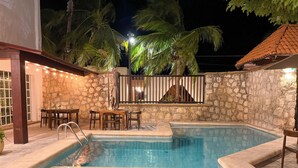 A swimming pool with stone walls, a wooden deck, and a bar area with chairs. - Progreso Beach Hotel (Progreso)