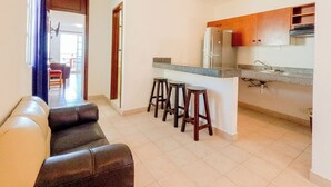 A modern kitchen with a refrigerator, sink, and bar stools. There is a leather couch in the living area. - Progreso Beach Hotel (Progreso)