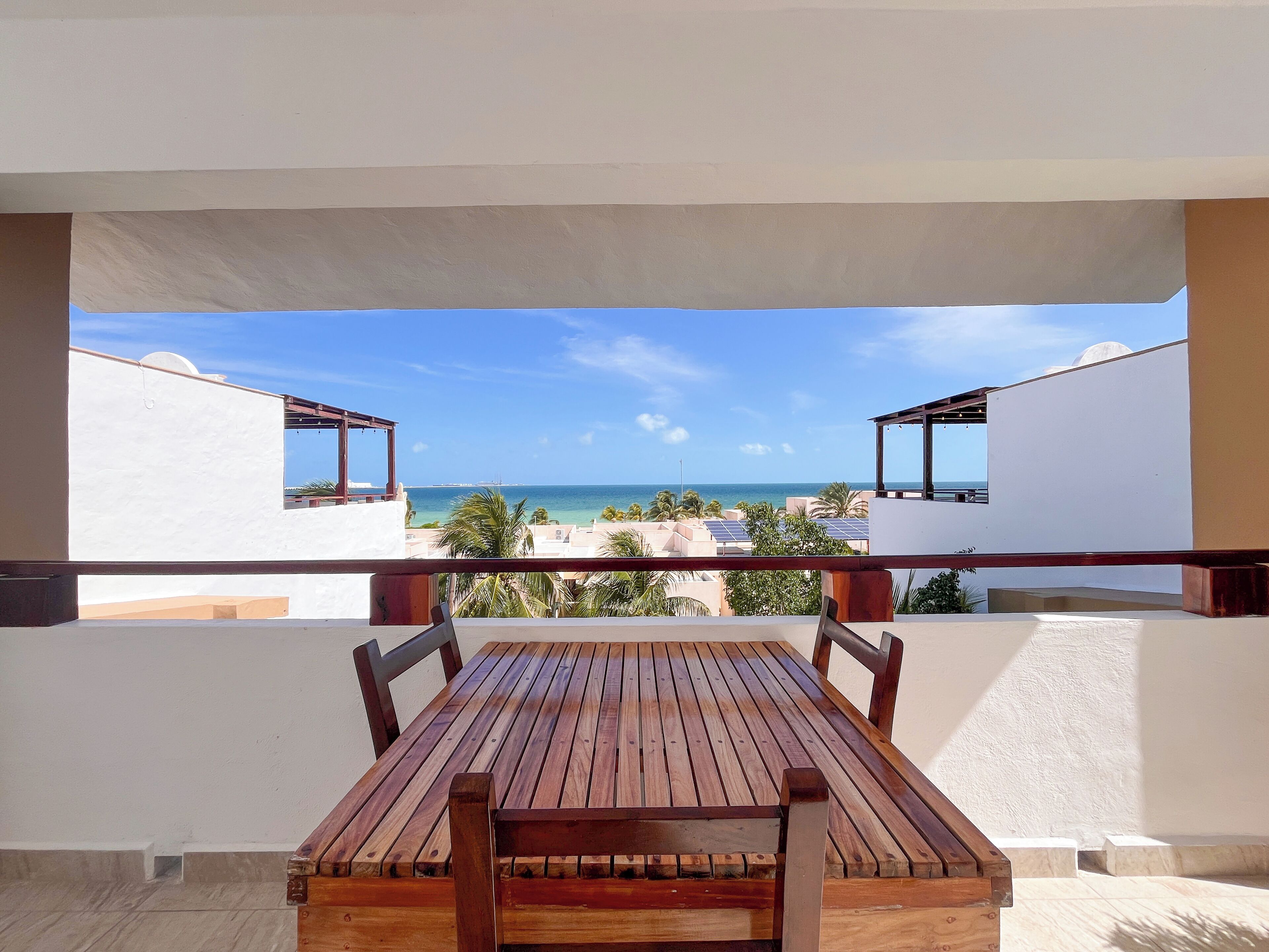 Una mesa y sillas de madera en un balcón con vistas al mar y edificios.