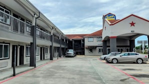 A hotel with a modern facade, multiple balconies, and a parking area with cars. - Scottish Inns and Suites East Sam Houston Pkwy (Houston)