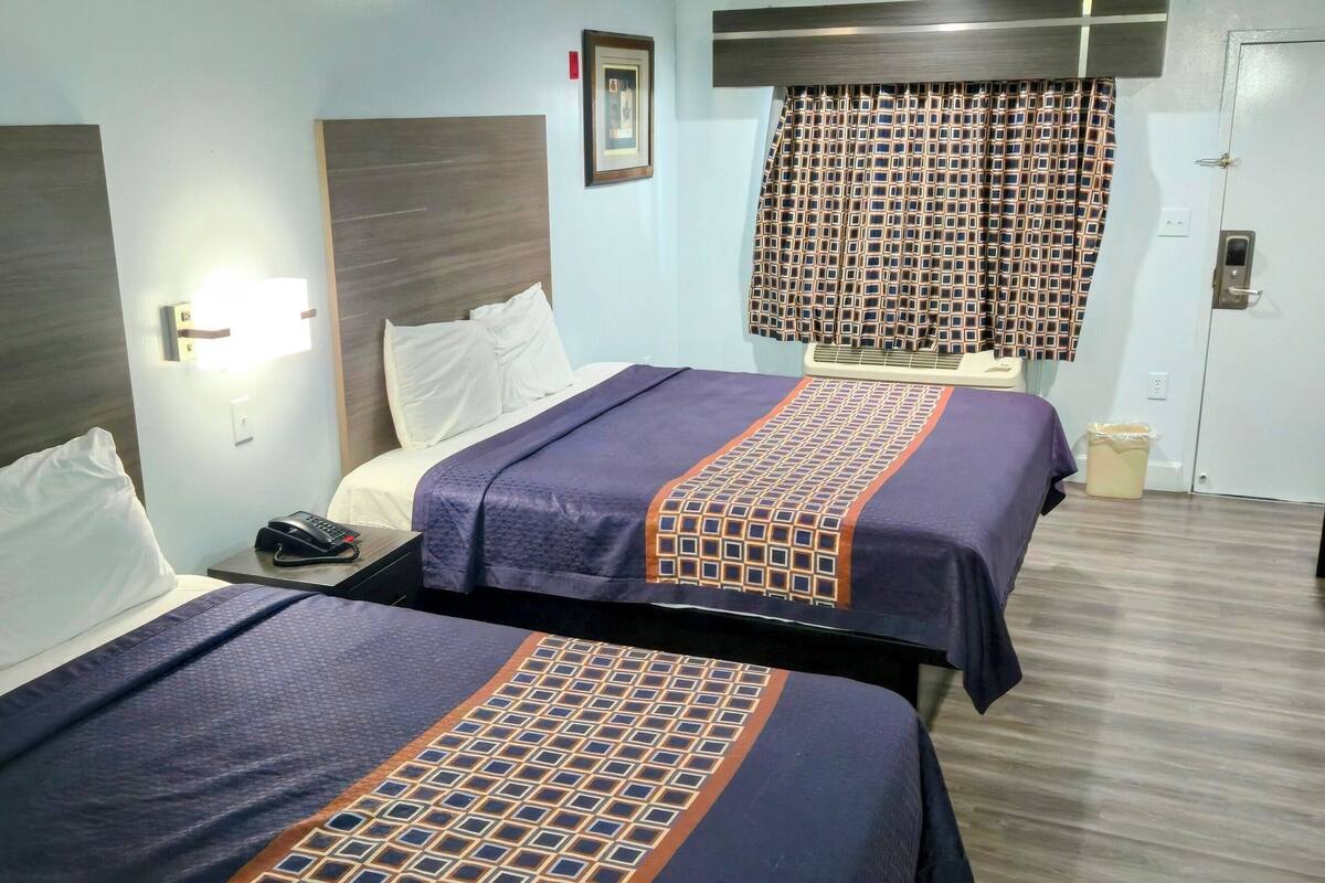 A hotel room with two beds, a desk, and a bathroom.