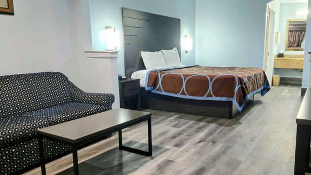 A hotel room with a bed, a sofa, a nightstand, and a table. - Scottish Inns and Suites East Sam Houston Pkwy (Houston)