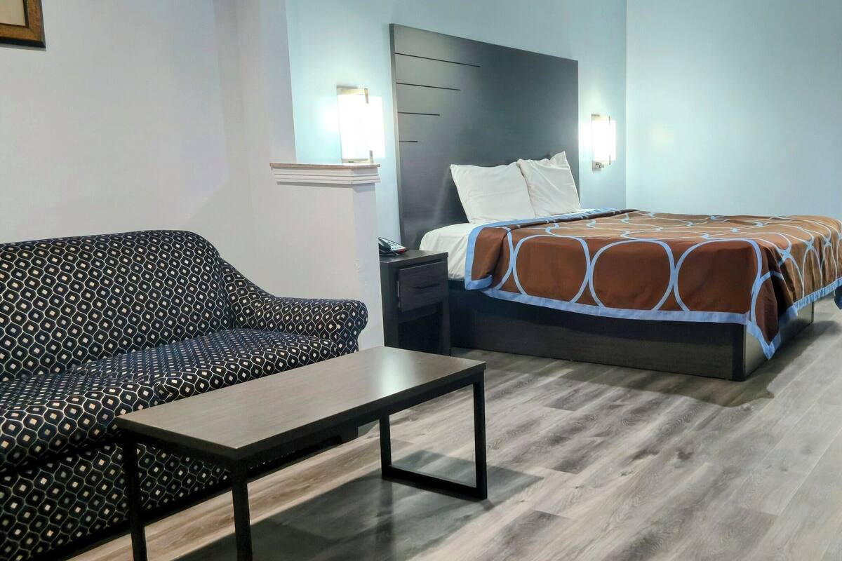 A hotel room with a bed, a sofa, a nightstand, and a table.