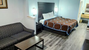 A hotel room with a bed, a sofa, a nightstand, a table, and a TV. - Scottish Inns and Suites East Sam Houston Pkwy (Houston)