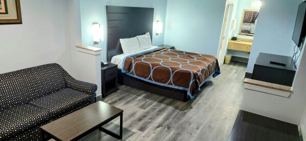 Quarto de hotel com cama, sofá, mesa de cabeceira, mesa e televisão.