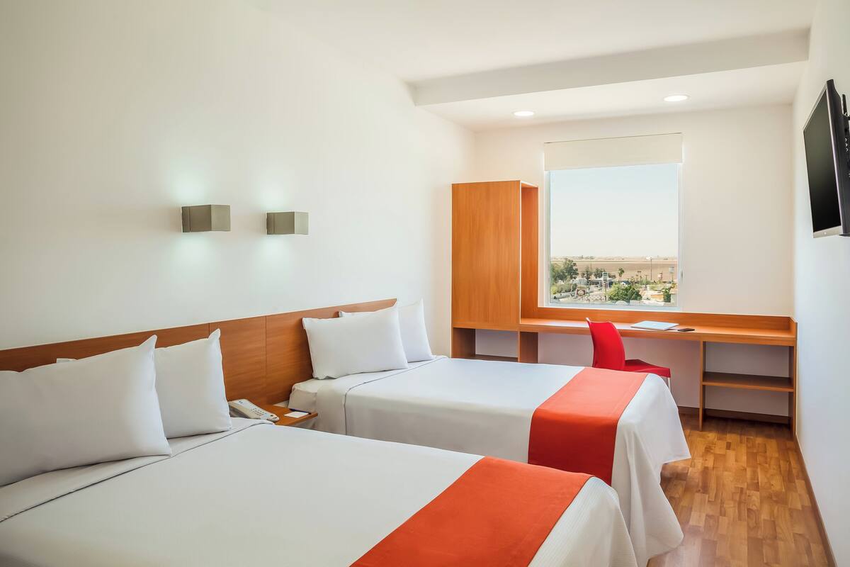A hotel room with two beds, a desk, a chair, and a large window with a view.