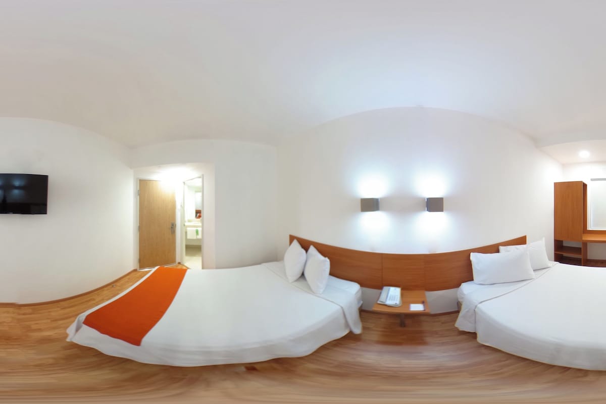 A hotel room with two beds, a TV, a wooden headboard, and a bedside table with a phone.