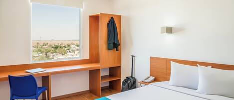 Una habitación de hotel con cama, escritorio, silla, maleta y vista a la ciudad.