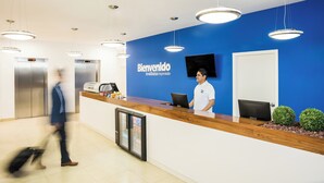 Un espace d’accueil avec un mur bleu, un comptoir de réception en bois, un écran numérique et un réfrigérateur.