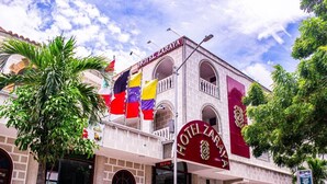 Un hotel con un letrero rojo llamativo, varias banderas y un balcón.