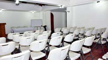 Un salón de conferencias con filas de sillas blancas, un atril, una pizarra y una puerta al fondo.