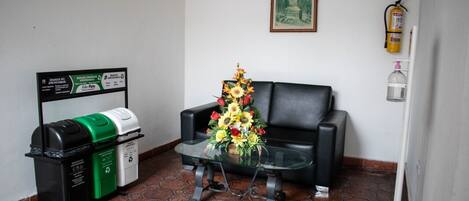 Una habitación con un sofá, una mesa de vidrio, un cubo de basura, un extintor y un cuadro en la pared.