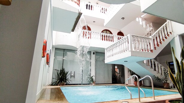 Una piscina interior con una fuente central, rodeada de balcones con barandillas blancas y detalles rojos.