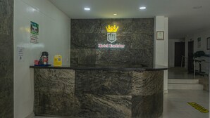Een hotel receptiebalie met een marmeren aanrecht, een logo met een kroon en een bord met een QR-code.