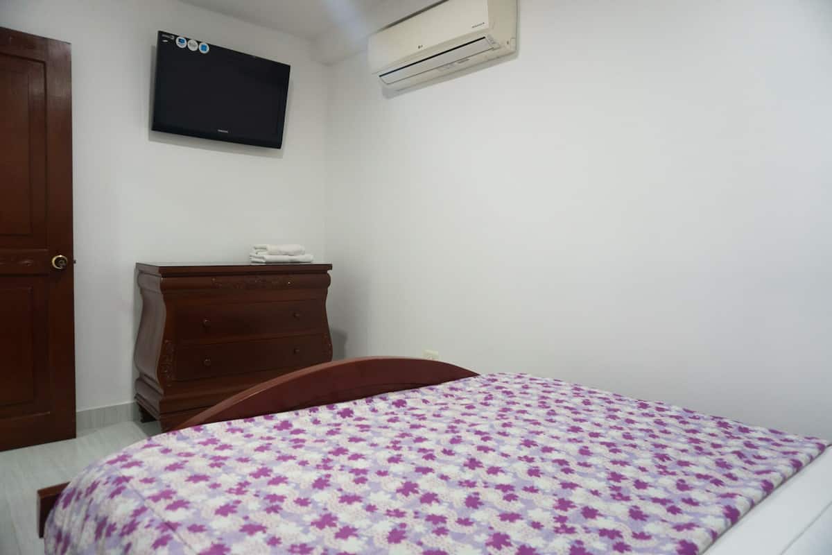 Un dormitorio con una cama, un aparador de madera, un televisor y un equipo de aire acondicionado.