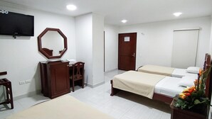 Een hotelkamer met een televisie, een houten dressoir, een spiegel, een bed met een beige sprei en een deur.