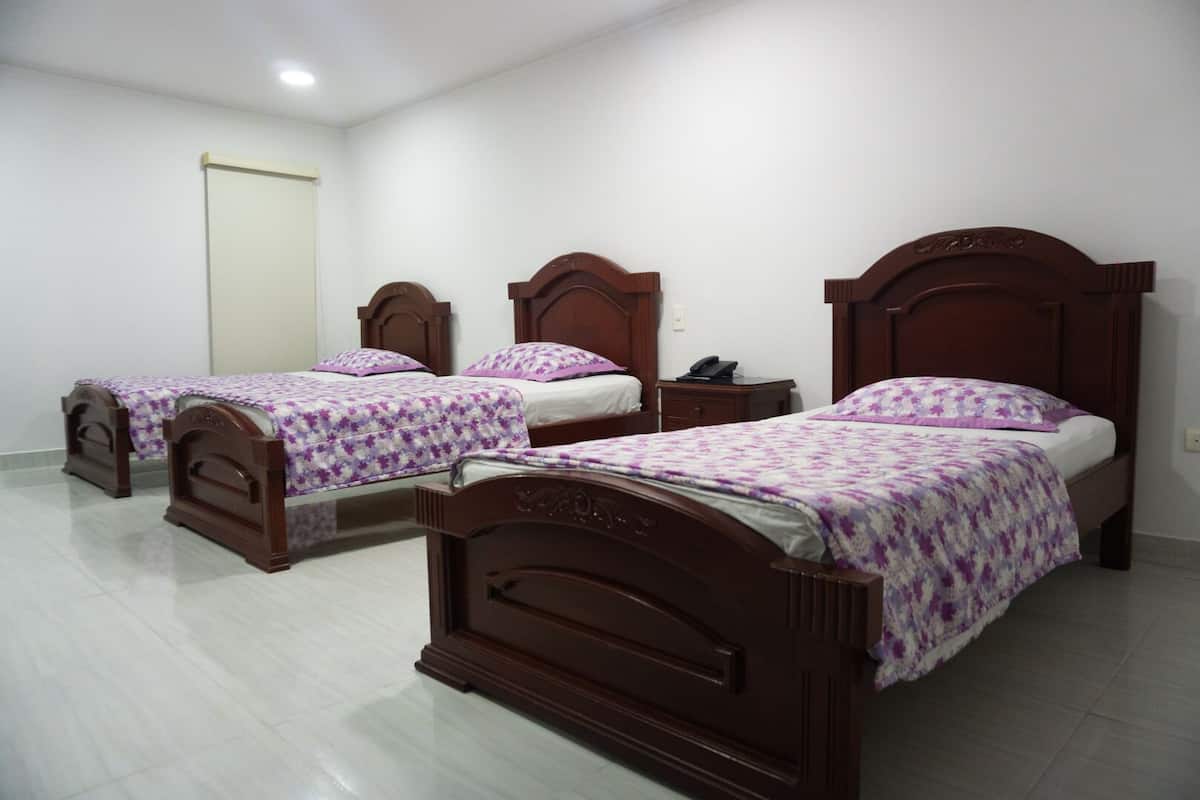 Habitación de hotel con tres camas de madera, cada una con una colcha floral púrpura.