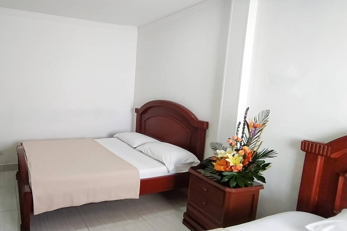 Un dormitorio con cama, cómoda, espejo y mesita de noche con un arreglo floral.