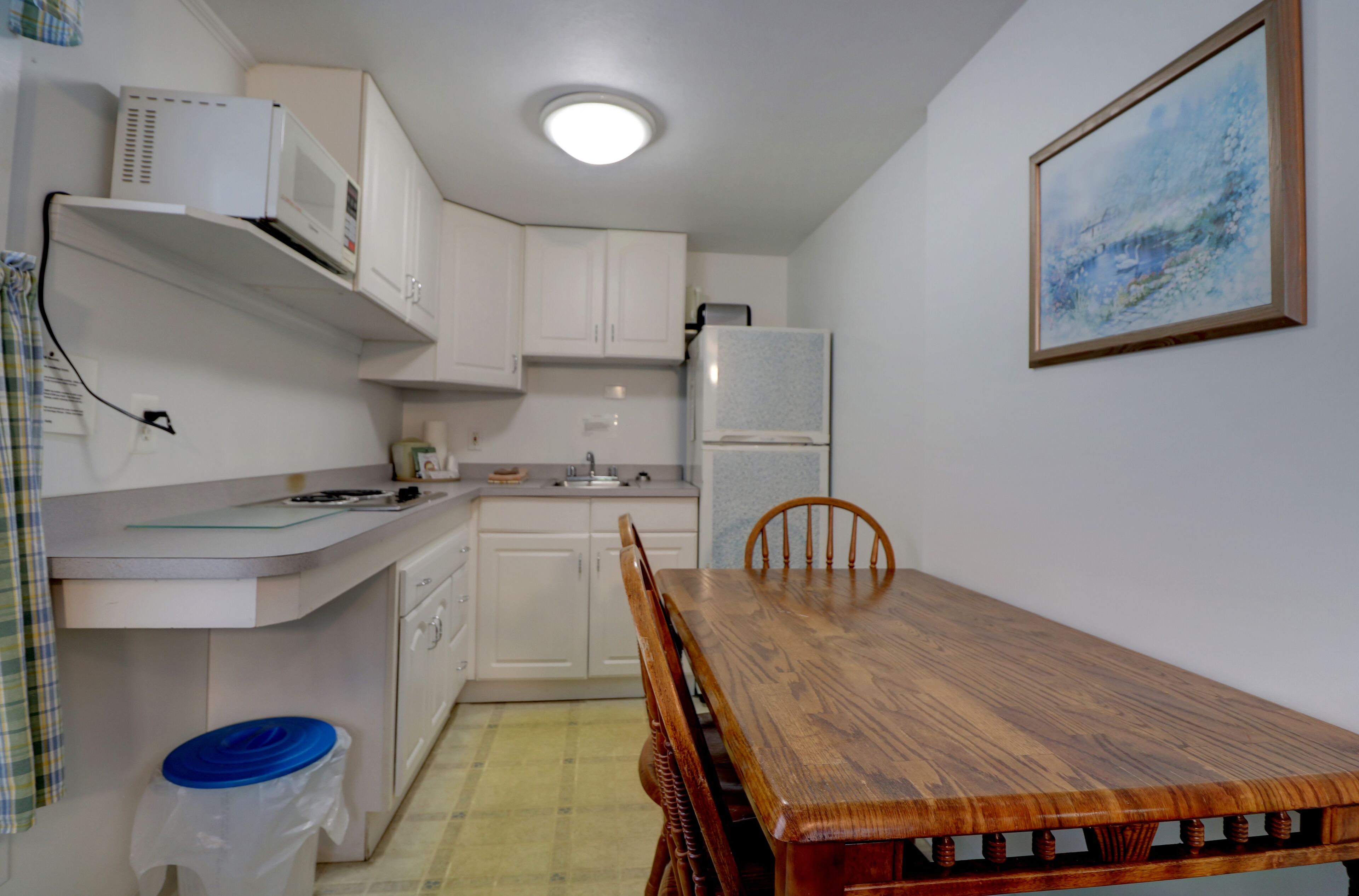 A compact kitchen with white cabinets, a wooden dining table, and a refrigerator.