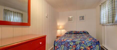 A bedroom with a red dresser, a floral bedspread, a mirror, and two framed pictures on the wall.