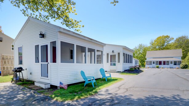 A mobile home with a porch, two blue chairs, and an American flag on the lawn. - Carriage House Motel Cottages & Suites (Wells)